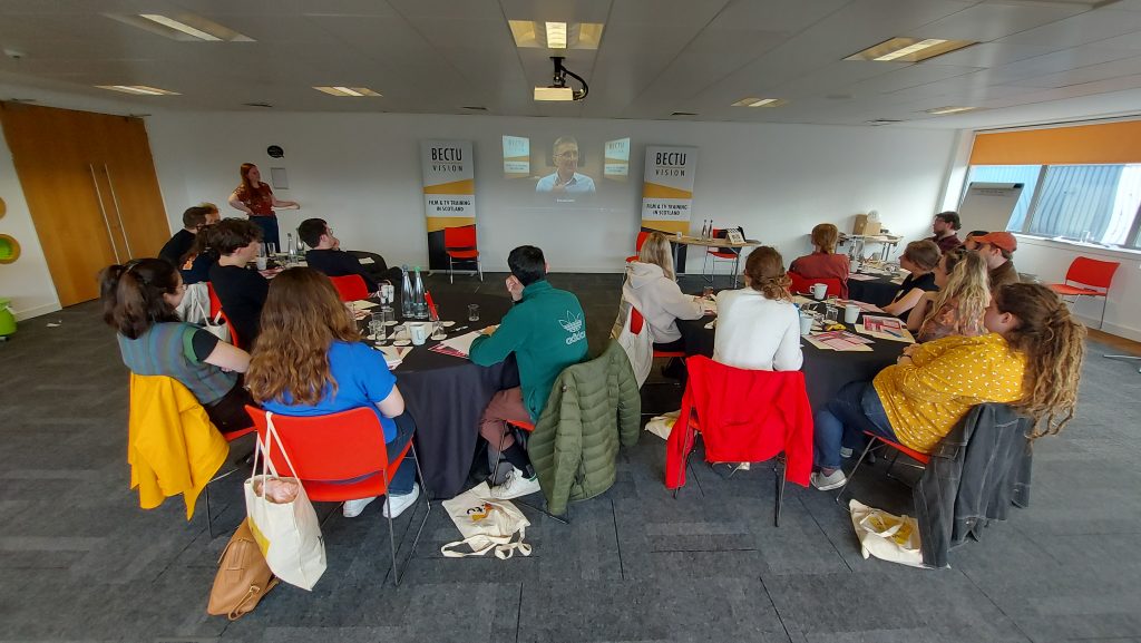 4 groups of 5 people sut around tables watching a presenter on screen. There are 2 BECTU Vision banners framing the screen.